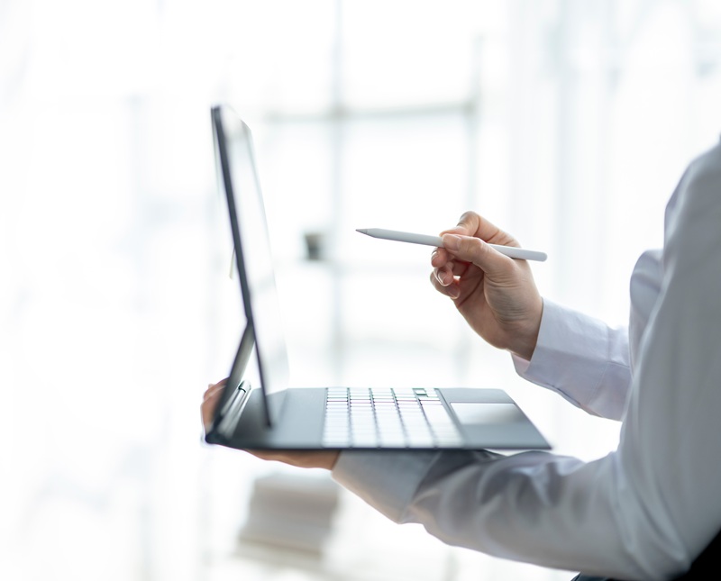 Image of a person holding a laptop and a pen in an office