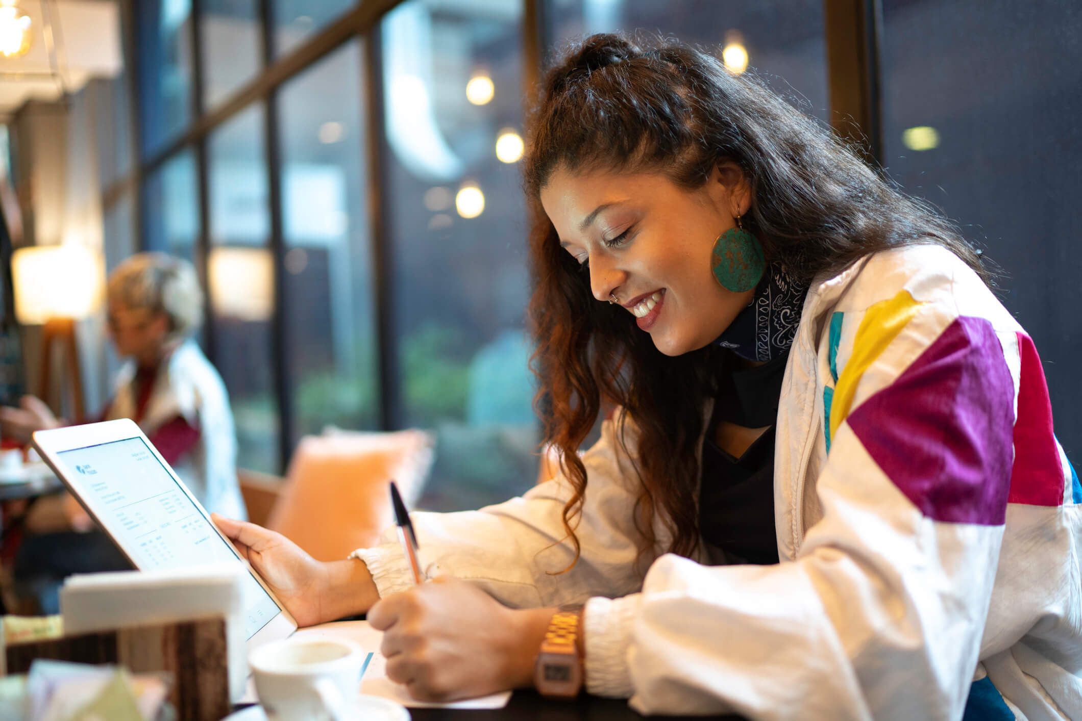 Young woman smiling as she writes down notes while holding an iPad