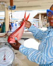 A female worker in a fish shop in Barbados, showing a flying fish, smiling at camera 