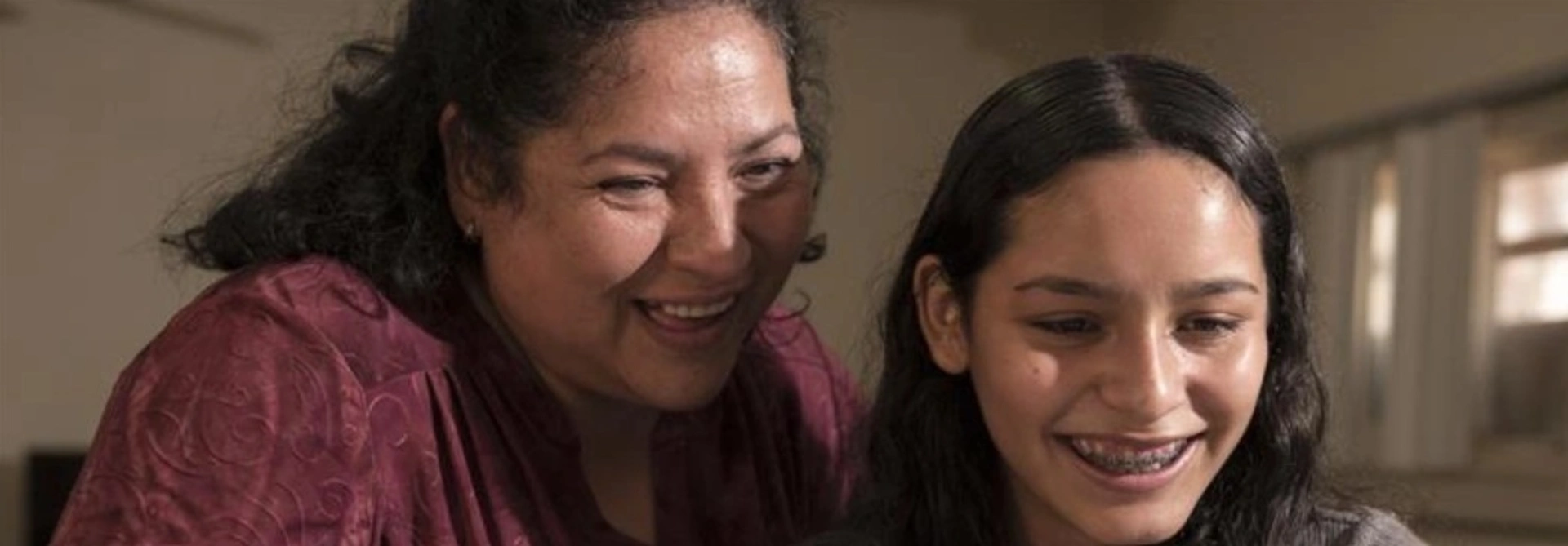 Image of an hispanic mom with her daughter smiling while looking at their computer connected to internet