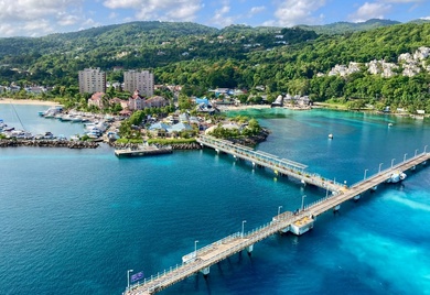 A vibrant coastal scene featuring a turquoise-blue bay with a long pier extending into the water