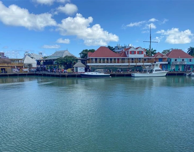 The image shows a waterfront scene with calm water in the foreground and a row of colorful buildings along the shore in the background.