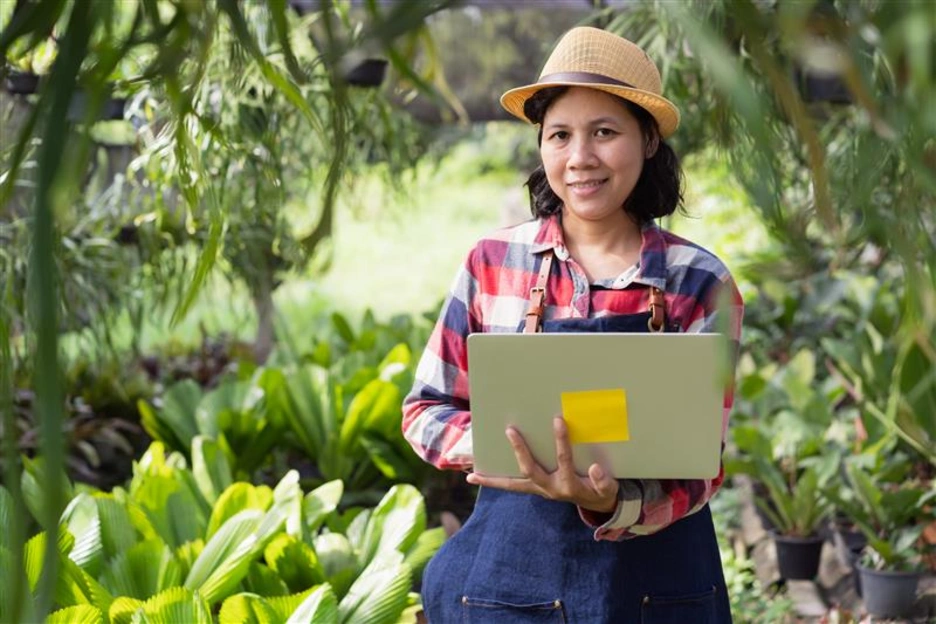 Woman happy and smiling while standing holding laptop in the Ornamental plant shop outdoor and looking to camera
