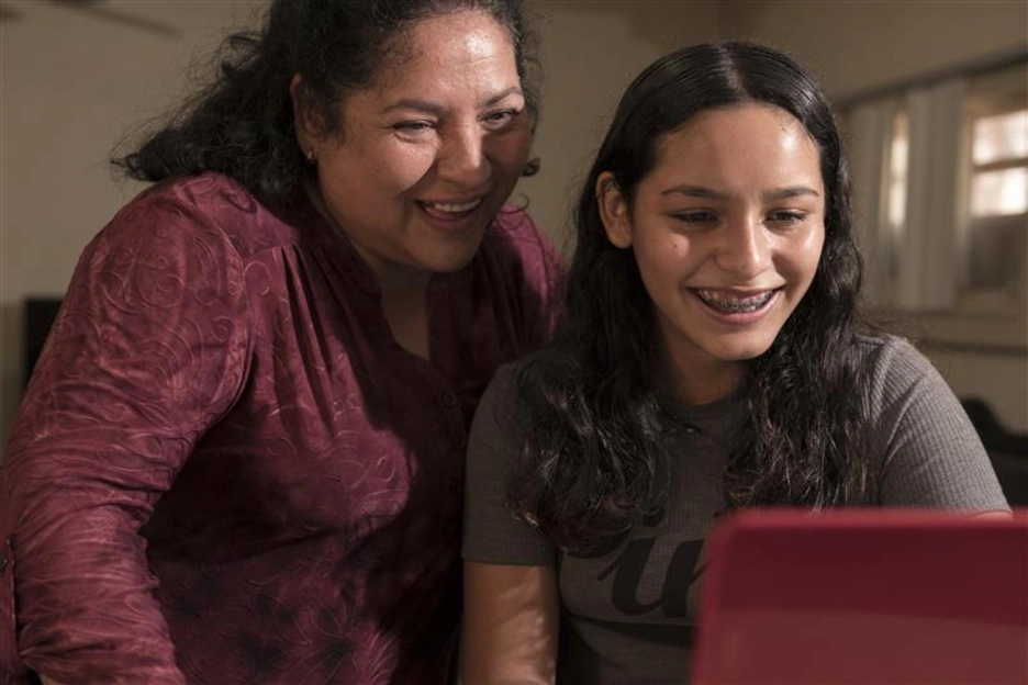 A mother and a daughter looking at a tablet and smiling