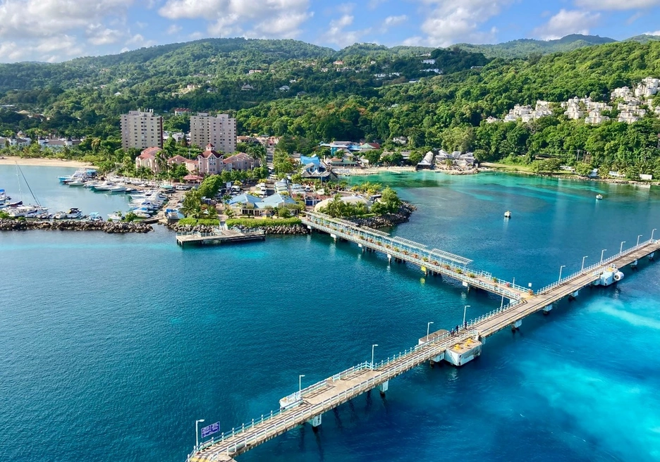 A vibrant coastal scene featuring a turquoise-blue bay with a long pier extending into the water